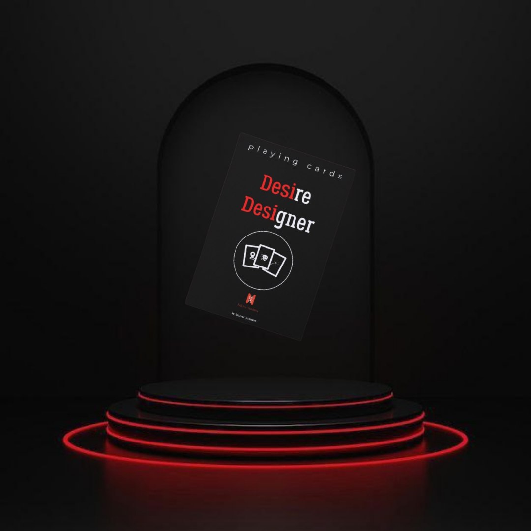 A dark promotional display showing a card deck box labeled 'Desire Designer' with red and white text, placed on a black tiered pedestal with glowing red ring lights against a black background.